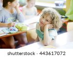 Small photo of The fair-haired curly schoolboy sits at a school desk in a class. The boy props up the head a hand and looks in the camera. The chappy has a good mood.