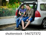 Small photo of Two young men drink beer from bottles. They have conveniently settled down in an open luggage carrier of the car. Friends derive pleasure from beer and communication.