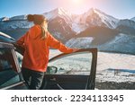 Woman traveling exploring, enjoying the view of the mountains, landscape, lifestyle concept winter vacation outdoors. Female standing near the car in sunny day, travel in the mountains.