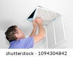 Mature man taking out a dirty air filter from a home ceiling air return vent. Male removing a dirty air filter with both hands in a house from a HVAC ceiling air vent.