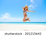 Portrait of young beautiful girl at tropical beach for vacations, jumping mid-air for joy, looking at camera and smiling. Copy space