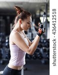 Small photo of Young slim woman doing pushdown on cable machine in gym. Athletic girl training triceps in fitness center