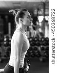 Small photo of Young slim woman doing pushdown on cable machine in gym. Athletic girl training triceps in fitness center. Black and white image.
