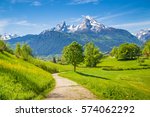 Beautiful view of idyllic landscape with scenic hiking trail in the Alps with fresh green mountain pastures and snow-capped mountain tops in the background in summer, Berchtesgadener Land, Bavaria