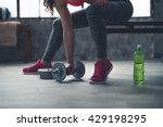 Body and mind workout in loft fitness studio. Closeup on fitness woman taking dumbbell from the floor in urban loft gym