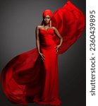 Small photo of Fashion Woman in Red Dress and Hijab. African Model in Evening long Gown with flowing Silk Fabric over Dark Gray background. Muslim Bride in Wedding chiffon Veil