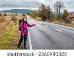 Travel woman hitchhiking. Beautiful young female hitchhiker by the road during mountain trip. Travel and vacation theme