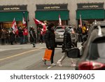 Small photo of Vancouver, BC, Canada, February 5, 2022, The asian pedestrians in the Burrard street with orange bag and masks with the blurry unmasked people with the Canadian flags on the background