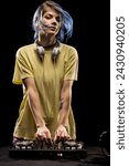 Small photo of Girl wearing headphones is focused on mixing music on a soundboard. Female DJ with blue hair and yellow t-shirt.