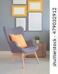Small photo of Retry style armchair with orange pillow in living room with wall of picture frame in background