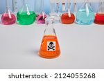 Small photo of Orange toxin vial on a chemical desk. Colorful flasks with bright elixirs. Colored liquids in chemical flasks and retorts. Mortal symbol on glassware. Fake orange juice. Danger poison orange agent.
