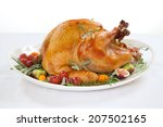 Roasted turkey on tray garnished with red grapes, figs, kumquat, and herbs over white background 