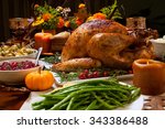 Roasted turkey garnished with cranberries on a rustic style table decoraded with pumpkins, gourds, asparagus, brussel sprouts, baked vegetables, pie, flowers, and candles.