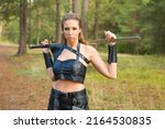 Small photo of medieval brigand lass wearing leather equipment with falchion in her hands defends the path in the forest