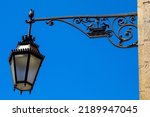 Small photo of Ornate street lamp in the historic city of Lisbon in Portugal. The design of the lamp shows a boat with two birds facing eachother - the symbol of the city.