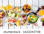 Healthy breakfast table scene with fruits, yogurts, oatmeal, cereal, smoothie bowl, nutritious toasts and egg skillet. Top view over a white wood background.