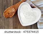 Greek yogurt in a heart shaped bowl, overhead scene against a rustic wood background