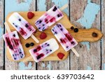 Homemade mixed berry yogurt popsicles on a paddle board with rustic wood background