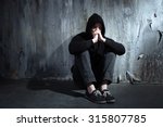 Photo of desperate young drug addict wearing hood and sitting alone in dark