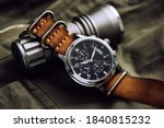 Close up black dial military style wristwatch with black leather watch band. Wristwatch for men with military objects in the background.