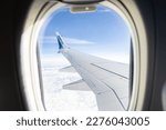 Small photo of Exact location unknown - February 11, 2023: Looking through an airborne WestJet passenger jet window at wing against blue sky and hilly terrain.