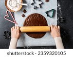 baking, cooking and christmas concept - close up of hands rolling gingerbread dough with rolling pin on black kitchen table top