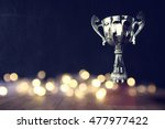 low key image of trophy over wooden table and dark background, with abstract shiny lights