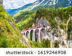 Glacier express on Landwasser Viaduct, Switzerland. It is landmark of Swiss Alps. Red Bernina train runs on railroad bridge in mountains. Aerial scenic view of railway in summer. Nice Alpine landscape