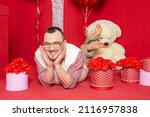 Funny happy bearded retro style man in the white vest lying down near gift boxes and big teddy bear for Valentine day