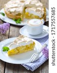 Small photo of Delicious rhubarb cake topped with sweet meringue and a cup of cappuccino served on a wooden table with springlike lilac decoration