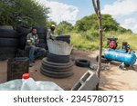 Small photo of african american street hustlers behind a compressor, fixing and inflating tires for a living, team of workers in workwear