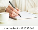 Woman writing in spiral notepad placed on bright desktop with coffee cup. Education concept
