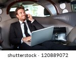 Smiling handsome businessman sitting in luxury limousine, working on laptop computer, smiling.