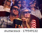 Happy couple sitting in movie theater, watching 3D movie, eating popcorn, smiling.