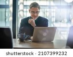 Small photo of Business portrait - businessman sitting in in office working with laptop computer. Mature age, middle age, mid adult man in 50s with happy confident smile. Copy space.