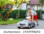 Two happy children playing with big old toy car in summer garden, outdoors. Kid boy pushing and driving car with little toddler girl, cute sister inside. Laughing and smiling kids. Lovely family