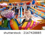 Adorable little preschool girl with glasses riding on animal on roundabout carousel in amusement park. Happy healthy baby child having fun outdoors on sunny day. Family weekend or vacations