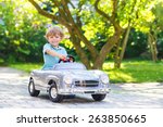 Little preschool boy driving big toy old vintage car and having fun, outdoors. Active leisure with kids on warm summer day.