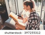 Young pretty woman  sitting at opened window drinking coffee and reading a book enjoys of rest