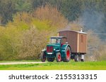 Oldtimer vintage agricultural tractor towing a wooden cabin trailer on a country road.