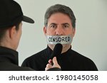 Censored eyewitness attractive adult person man, (male age 40-50) with mouth shut with tape, being interviewed by fake news reporter.Freedom of the press and media concept. Real people. Copy space