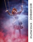 Small photo of Puppet theater and circus. Portrait of an actress dressed in vintage style playing a role of a doll on strings at a puppet theater performance. Full length portrait with magic red and blue smoke.