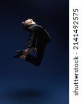 Small photo of The concept of success and aspirations, dreams. A man in a black classic suit jumps, striving for the heights. Studio full-length portrait on a dark blue background. Success in business.