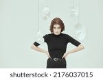 Small photo of Theater of life. A girl in black clothes stands in a white room surrounded by various masks looking intently at the camera. Hypocrisy. Human roles. Mental disorders.
