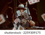 A tough gangster man in an elegant black suit and a white hat sits in a luxury apartment and plays cards. Retro style. Detective movie. The criminal world of the mafia. 
