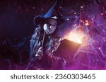 Small photo of Magic Halloween spells. Beautiful curly-haired sorceress in a black hat makes a spell with a magical book and a wand in a dark old castle covered in cobweb. Art of witchcraft.
