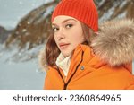 Portrait of a fashionable girl posing in orange ski suit against a snowy winter landscape. Winter fashion. Winter sport in the mountains.