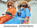 Winter holidays. Two beautiful girls in bright downy overalls enjoy their vacation at the ski resort. Alpine skiing, winter activities.