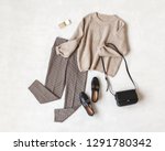 Brown pants in check, beige knitted oversize sweater, cross body bag, black loafers or flat shoes on grey background. Overhead view of women's casual day outfit. Flat lay, top view. Women clothes.