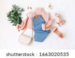 Blue jeans, pink knitted sweater, heeled sandals, small bag and bouquet of flowers lie on white background. Overhead view of woman's casual outfit. Trendy stylish women clothes. Flat lay, top view.